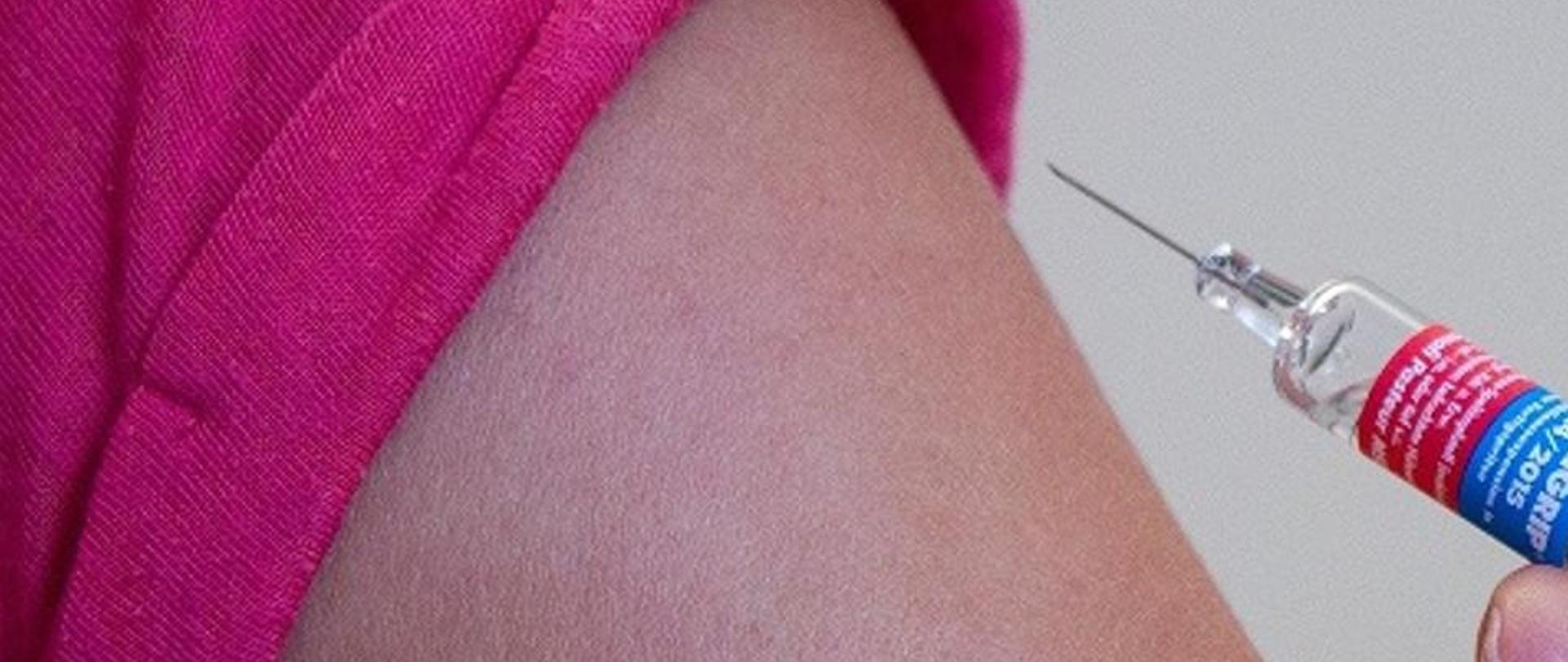 ręka przygotowana do szczepienia, a przy niej widoczna dłoń, trzymająca strzykawkę z igłą ze szczepionką przeciw grypie