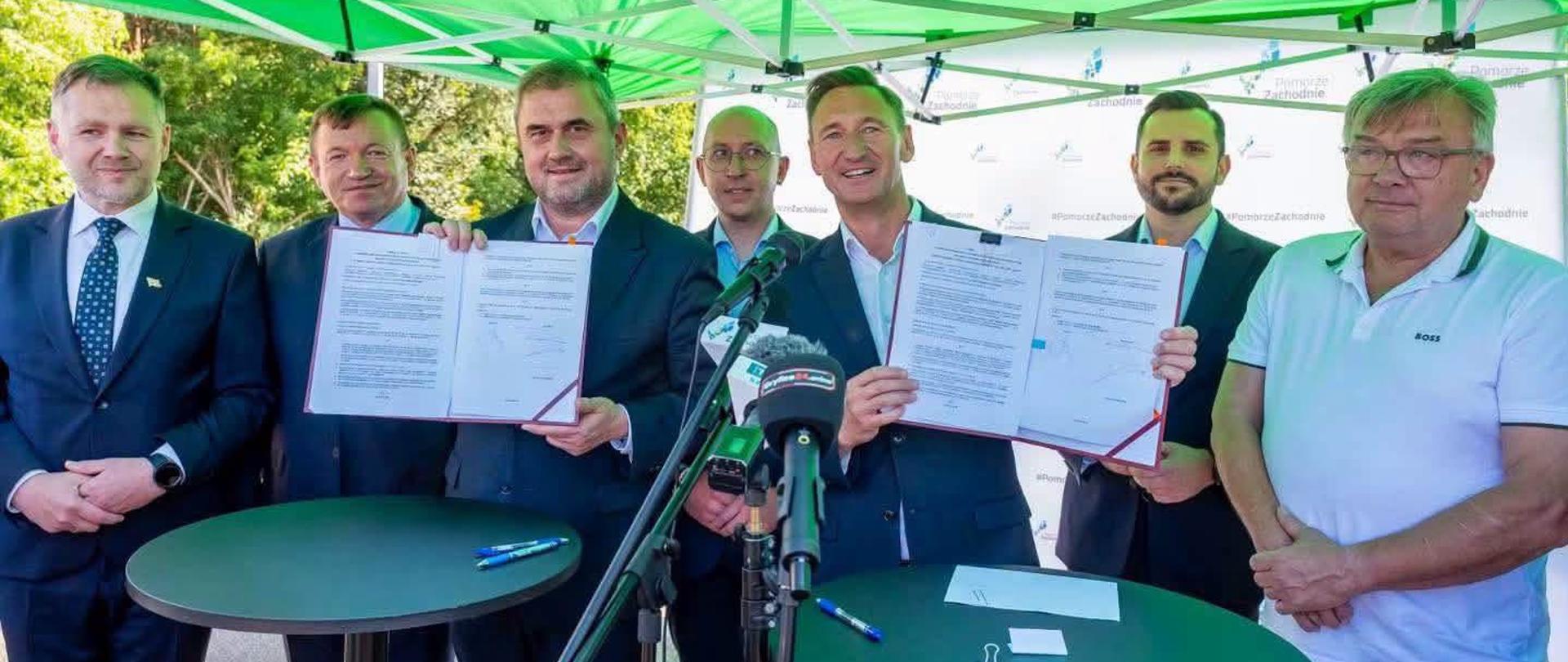wiceminister infrastruktury i marszałek województwa trzymają podpisane umowy, obok posłowie, z tyłu wicemarszałek i wicewojewoda
