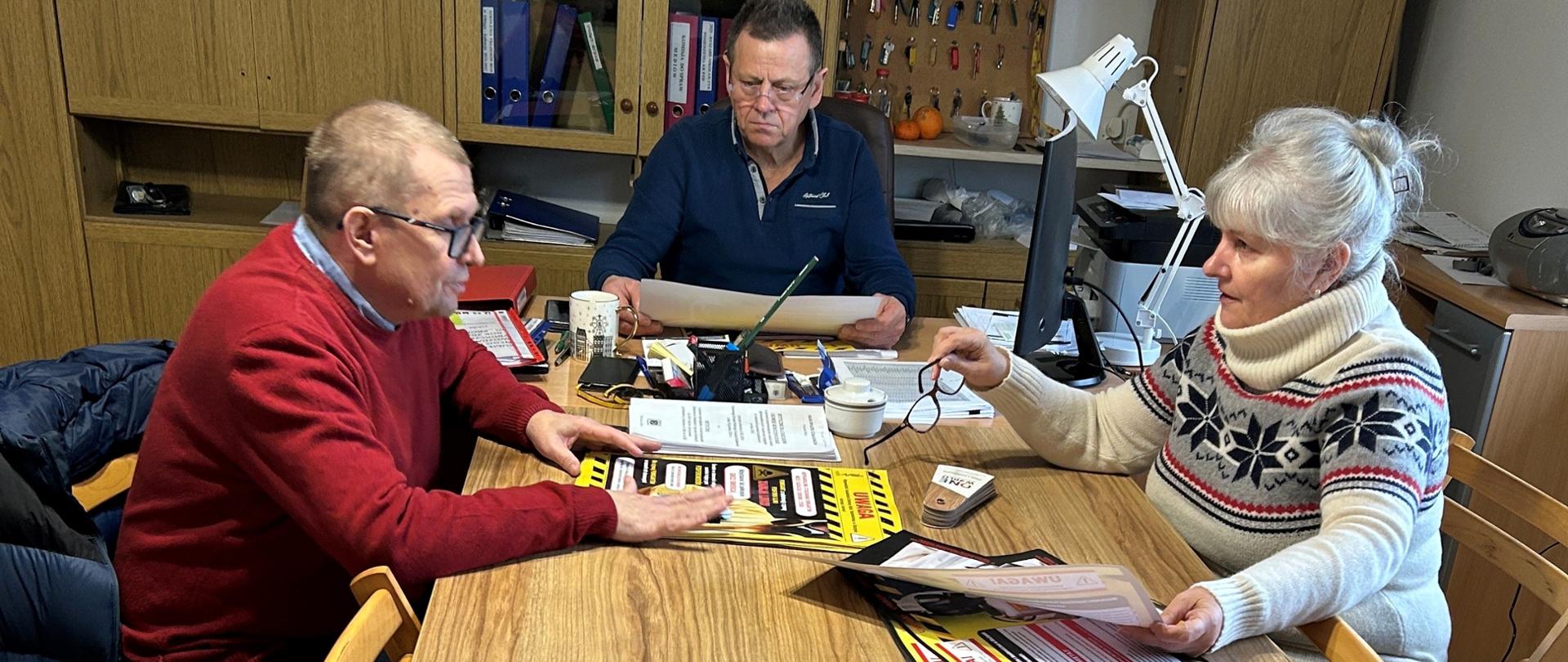 Spotkanie z Zarządem Okręgowym Polskiego Związku Działkowców w Elblągu. Troje uczestników siedzi naprzeciw siebie przy stole, na którym leżą plakaty o stosowaniu śor