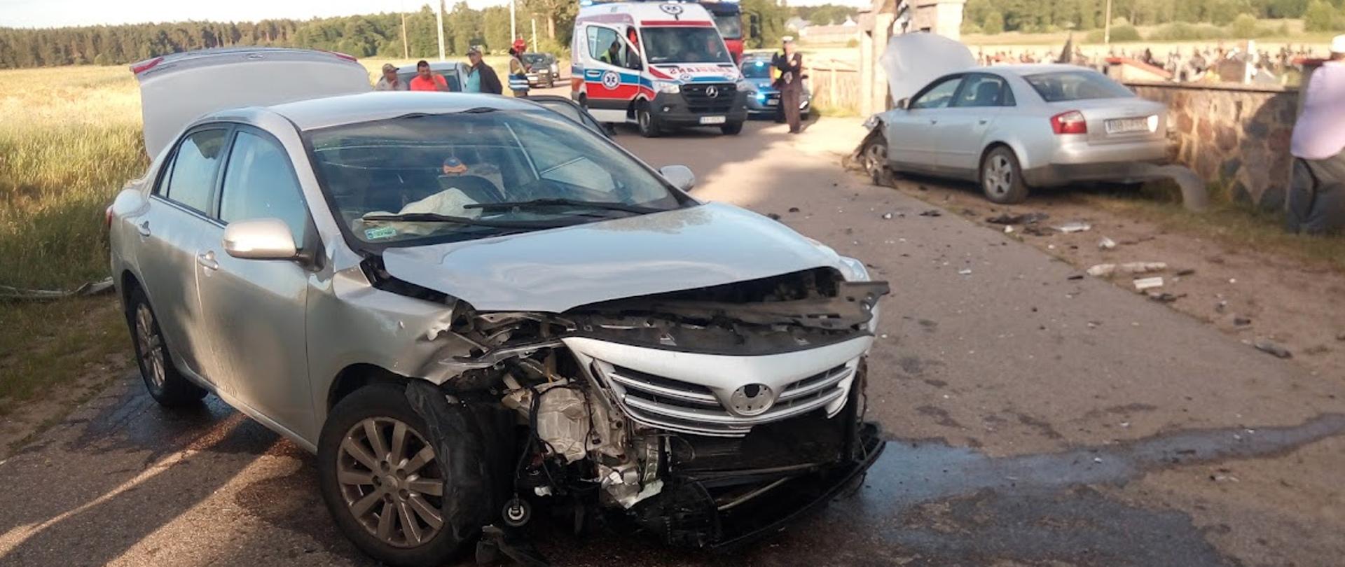 Zdjęcie przedstawia rozbity przód srebrnego auta osobowego na drodze z rozlanym płynem eksploatacyjnym 