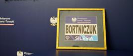 Na zdjęciu widać numer startowy Diamentowej Ligi z nazwiskiem Bortniczuk, oprawiony w złotą ramkę. Tło zdjęcia stanowi granatowa ściana z logotypem Ministerstwa Sportu i Turystyki, orłem oraz hasłem tworzymy polski sport. 