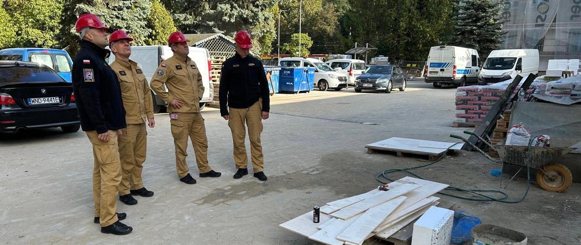 Na zdjęciu Mazowiecki Komendant Wojewódzki PSP nadbryg. Artur Gonera, zastępca Mazowieckiego Komendanta Wojewódzkiego PSP st. bryg. Piotr Gąska, Komendant Miejski PSP m.st. Warszawy st. bryg. Sławomir Sierpatowski i zastępca Komendanta Miejskiego PSP m.st. Warszawy st. bryg. Michał Płachta, ubrani w piaskowe mundury służbowe stoją na parkingu przed remontowanym obiektem.