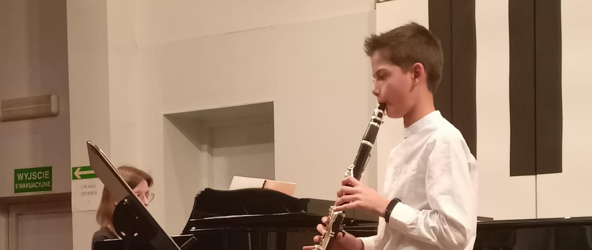 Chłopiec gra na klarnecie, kobieta akompaniuje mu na fortepianie.
