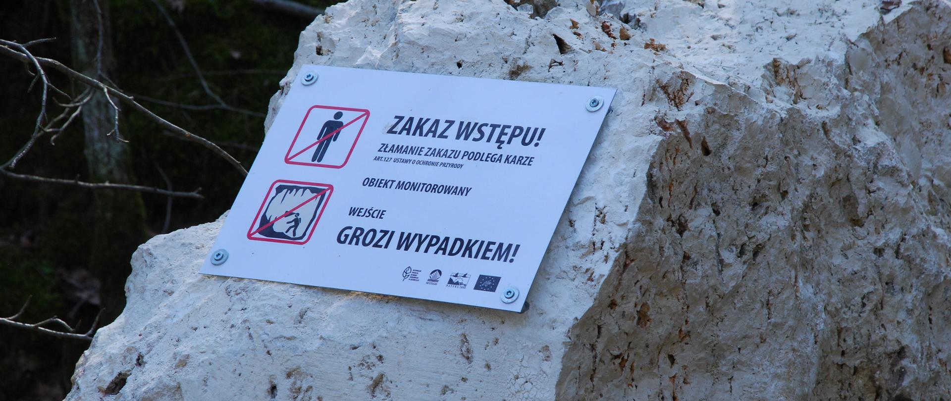 Zdjęcie przedstawia tabliczkę informującą o zakazie wstępu do jaskini w rezerwacie Szachownica