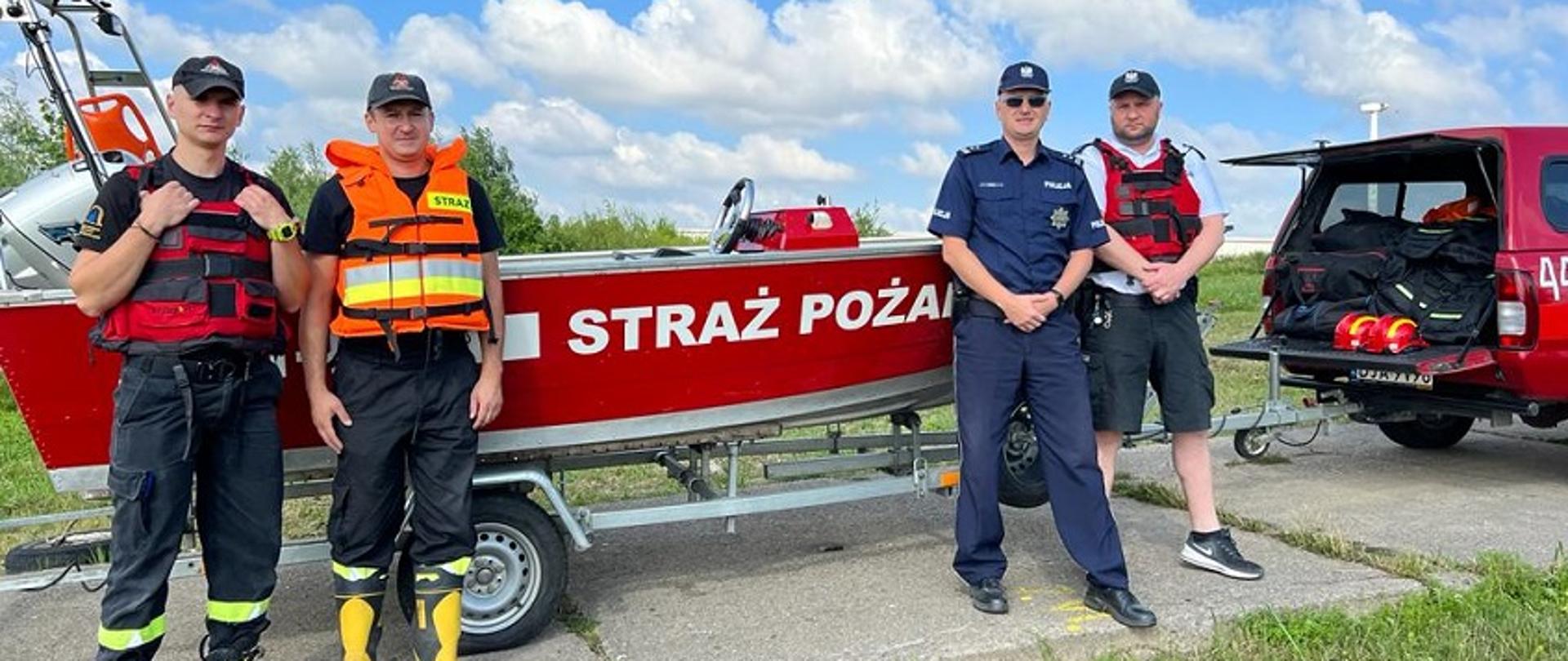 Obraz przedstawia strażaków i policjantów na tel łodzi ratowniczej