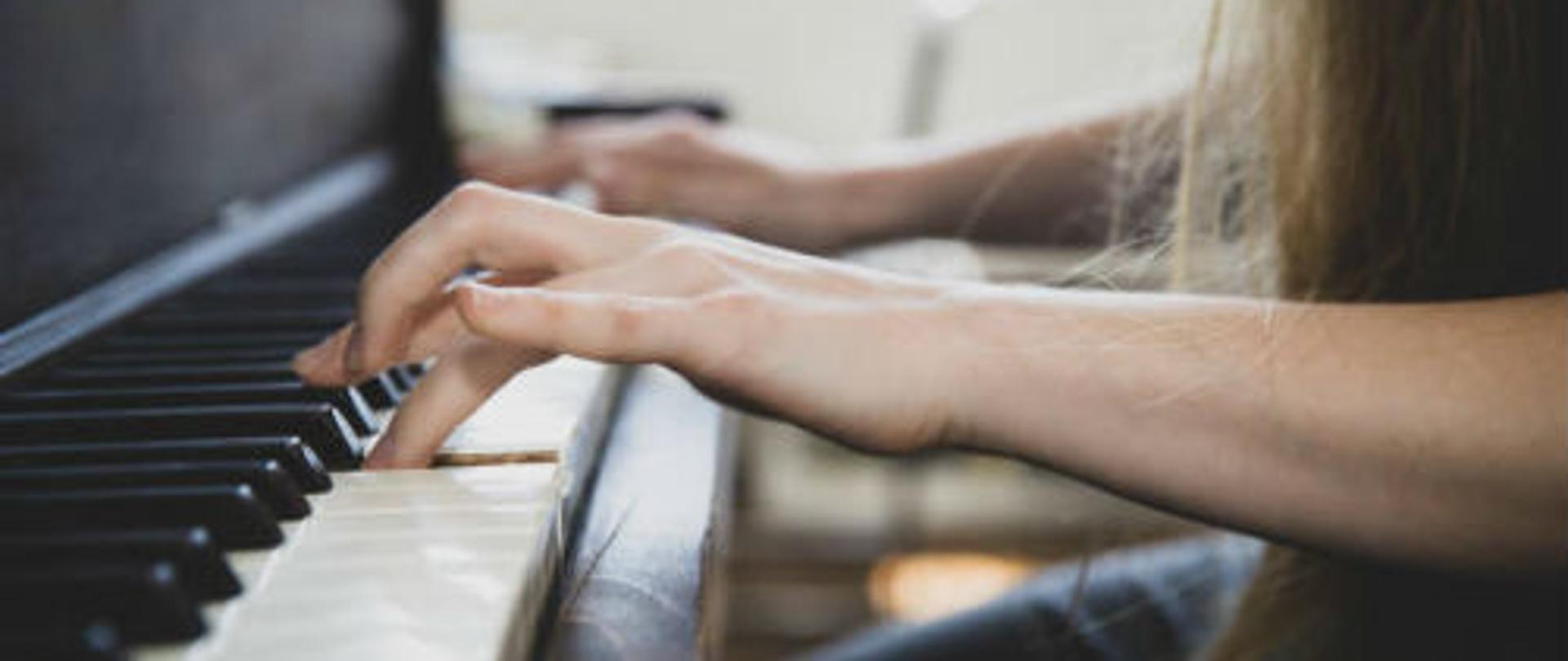 Zdjęcie przedstawiające dłonie dziewczynki grające na fortepianie