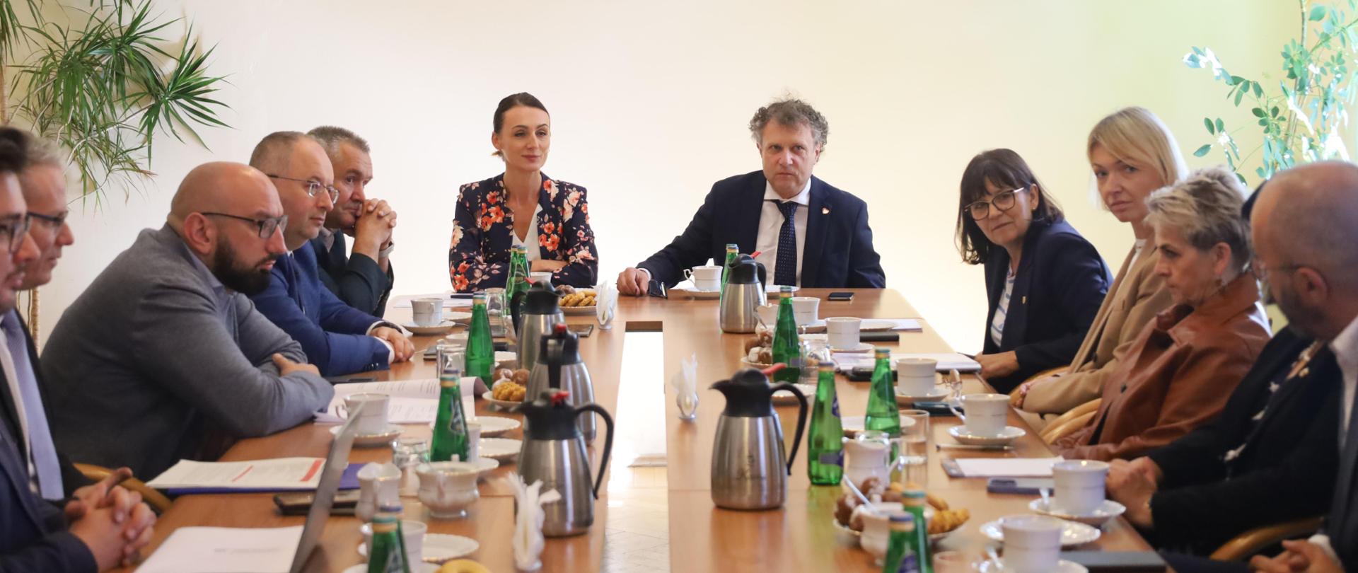 kilkanaście osób siedzi przy stole i dyskutuje