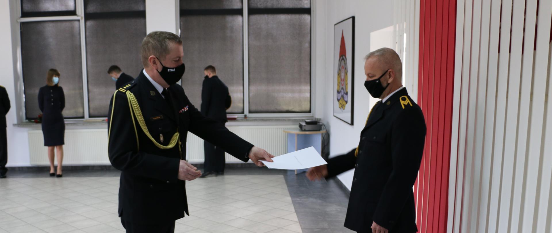 Dwóch strażaków - komendant wręczający dokument strażakowi emerytowi