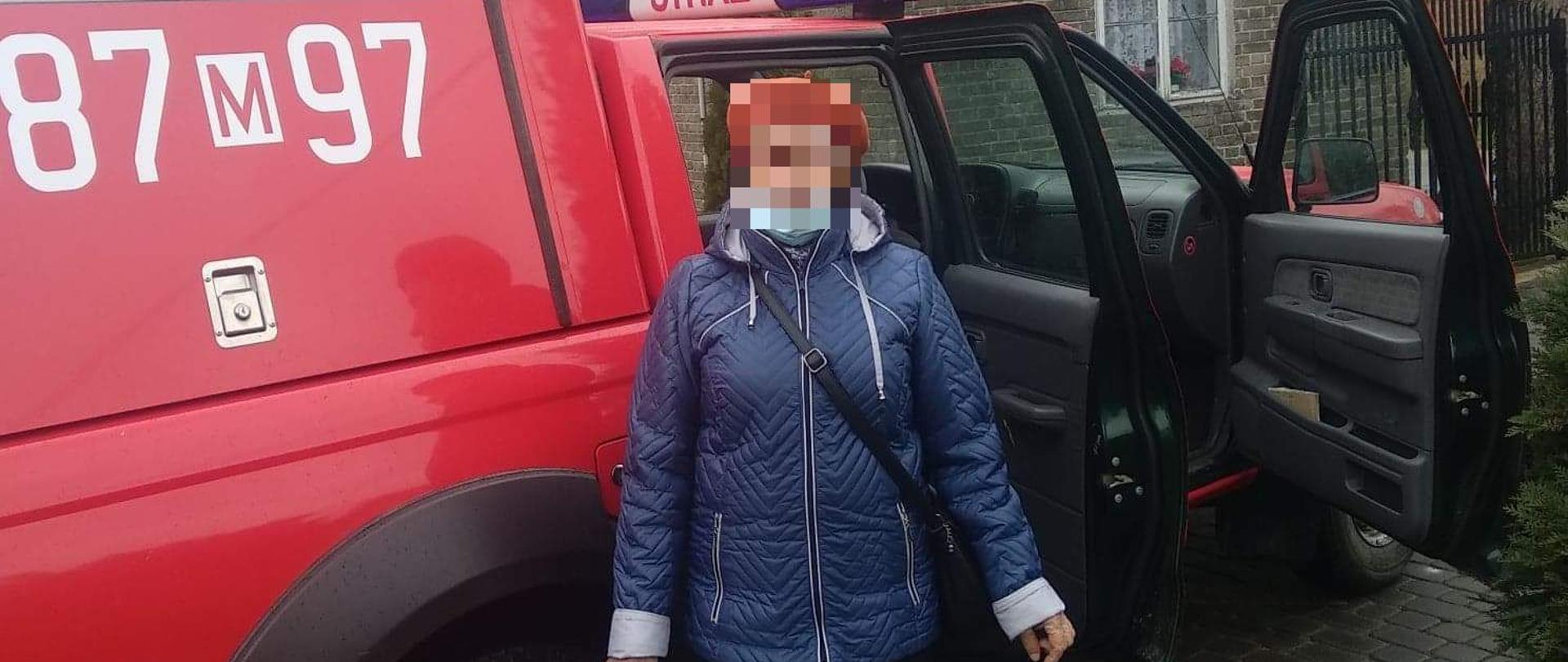 Na pierwszym planie na zdjęciu widać samochód OSP typu pic-up. Do środka wsiada kobieta, która ma założoną maseczkę na twarzy. 