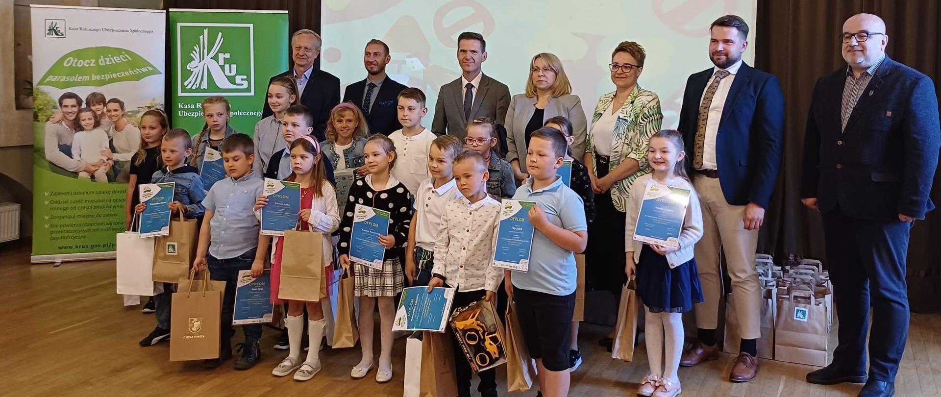 Wspólne zdjęcie grupy dzieci z dyplomami i nagrodami .Z tyłu za dziećmi stoi pięciu mężczyzn i dwie kobiety.