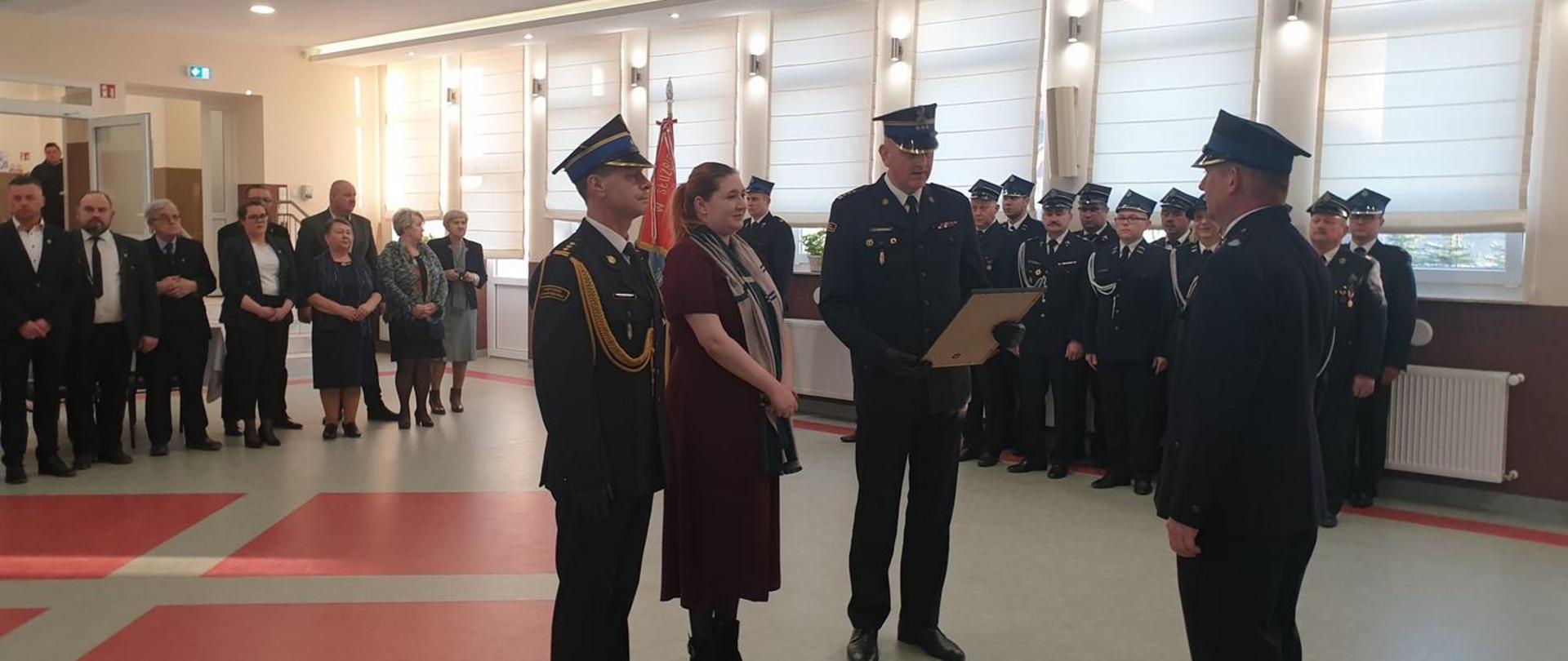 Zdjęcie przedstawia Panią Annę Gębicką – Sekretarz Stanu w Ministerstwie Rolnictwa i Rozwoju Wsi, Poseł na sejm RP, Zastępcę Kujawsko Pomorskiego Komendanta Wojewódzkiego PSP st. bryg. Sławomira Herbowskiego oraz Komendanta Powiatowego PSP w Brodnicy st. bryg. Andrzeja Góreckiego wręczających Decyzję Komendanta Głównego Państwowej Straży Pożarnej z dnia 6 grudnia 2021 r. o włączeniu OSP Bobrowo do Krajowego Systemu Ratowniczo-Gaśniczego. Na drugim planie zaproszeni na uroczystość goście i strażacy.