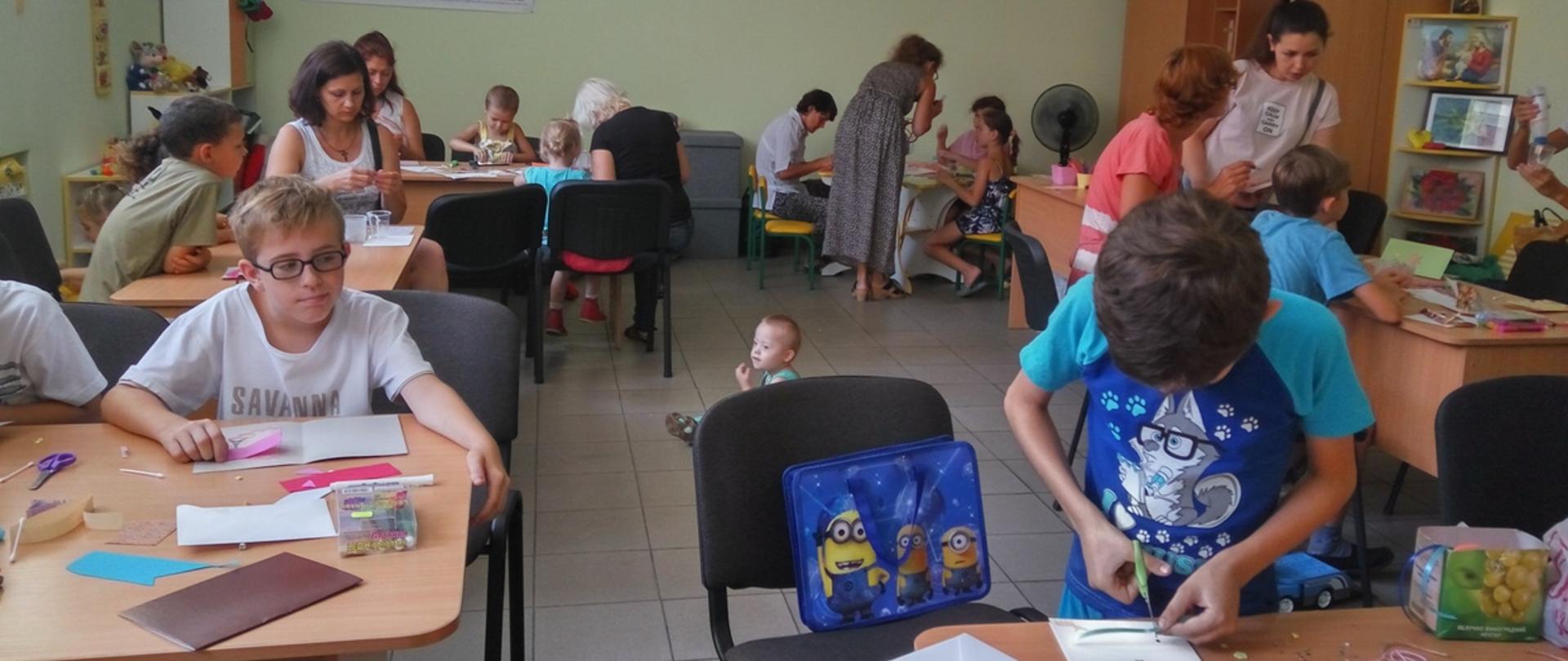 w świetlicy grupa dzieci wraz z opiekunami wycina karteczki i maluje obrazki