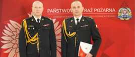Funkcjonariusze Państwowej Straży Pożarnej w umundurowaniu na czerwonym tle z wizerunkiem godła państwowego.