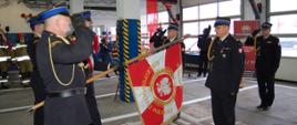 Zdjęcie przedstawia moment przekazania sztandaru Komendy Powiatowej Państwowej Straży Pożarnej w Brodnicy. Komendanci oddają honor sztandarowi Komendy. W tle pracownicy Komendy.