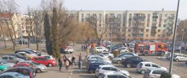 Zdjęcie w ciągu dnia. Na terenie kampusu UAM w Kaliszu. Widać pojazdy na parkingu, osoby postronne oraz pojazdy ratowniczo-gaśnicze. Zdjęcie wykonane podczas ćwiczeń.