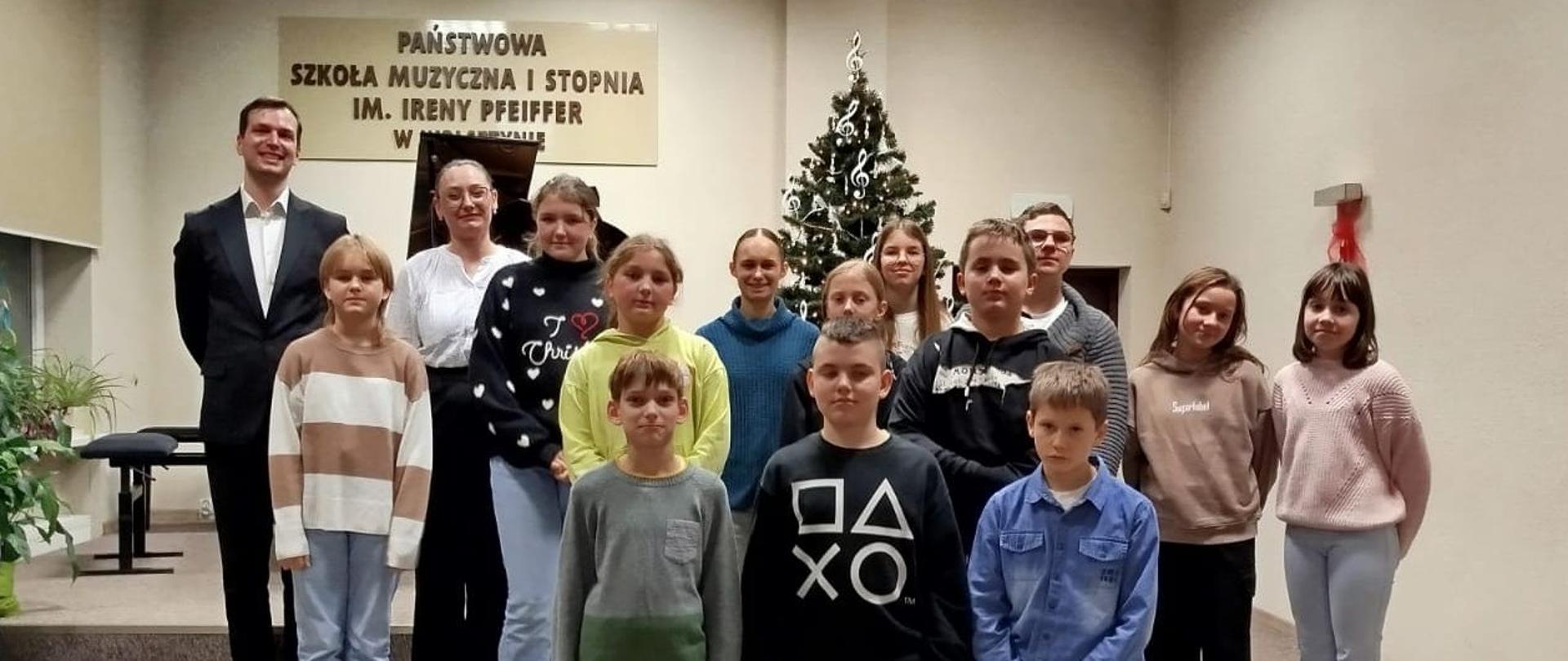 Na scenie stoi grupa uczniów. Wśród nich pan Jakub Czerski - grający utwory J. I. Paderewskiego.