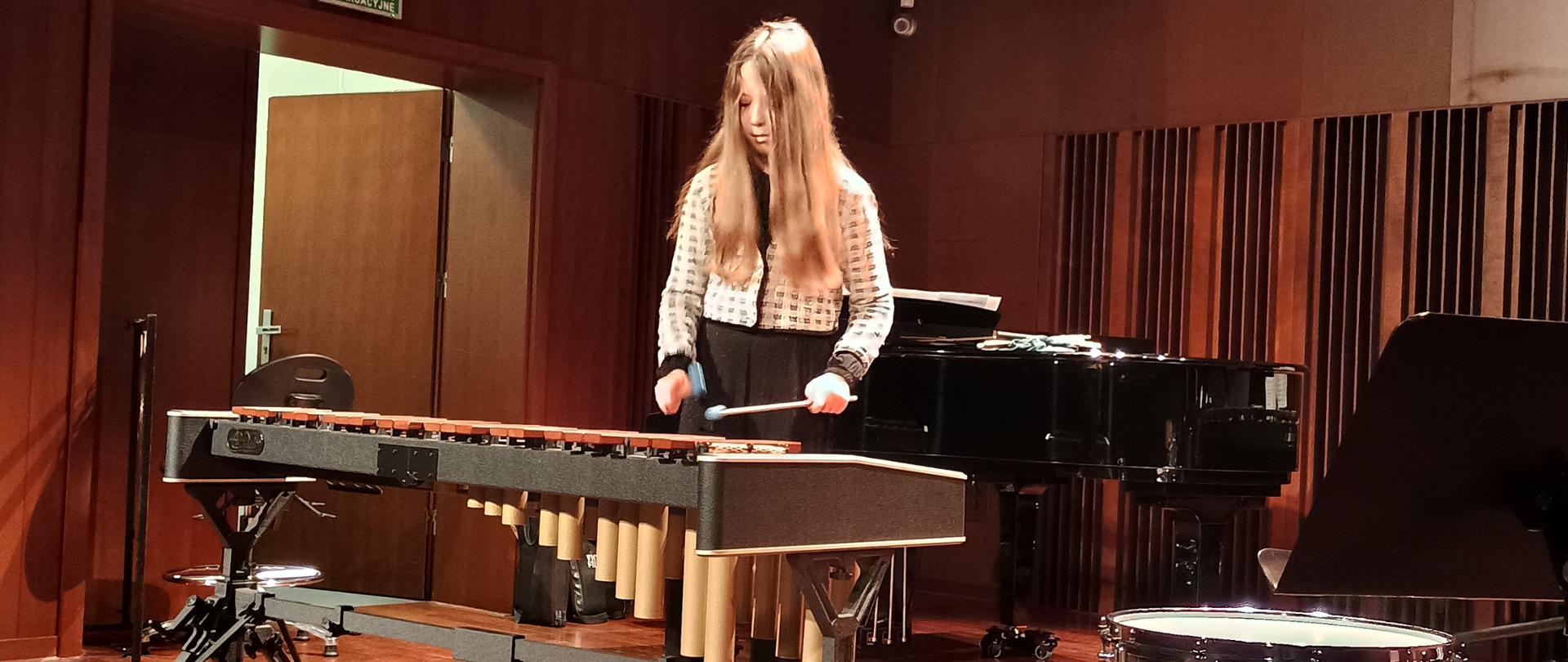 Warsztaty perkusyjne w szkole. Uczennica gra na marimbie na scenie sali koncertowej.