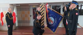 Zdjęcie przedstawia odchodzącego na emeryturę komendanta podczas pożegnania ze sztandarem Komendy Powiatowej PSP w Pruszczu Gdańskim.