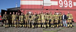 Pamiątkowe zdjęcie grupowe uczestników warsztatów dotyczących wykorzystania termowizji w działaniach gaśniczych na tle kontenera do ćwiczeń pożarów wewnętrznych
