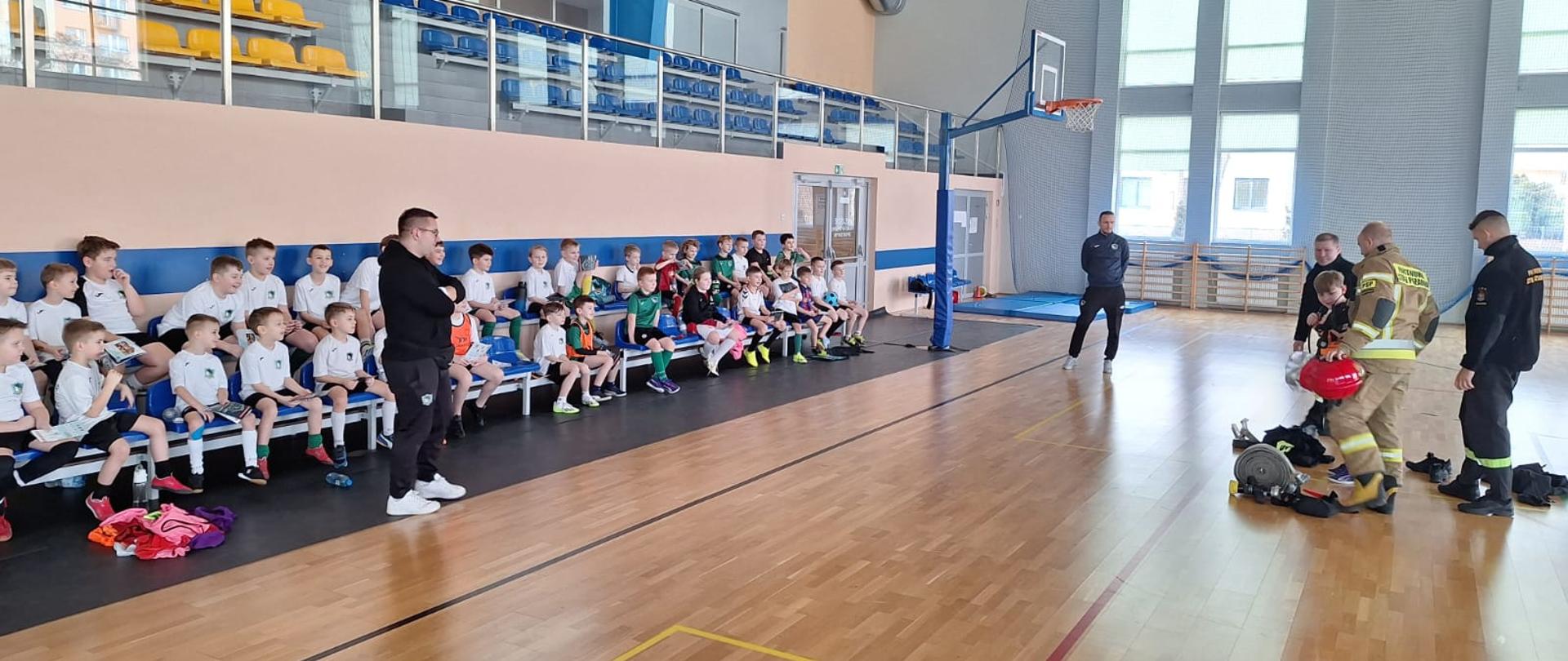 Dzieci wraz z opiekunami uważnie słuchają funkcjonariuszy KP PSP w Makowie Mazowieckim