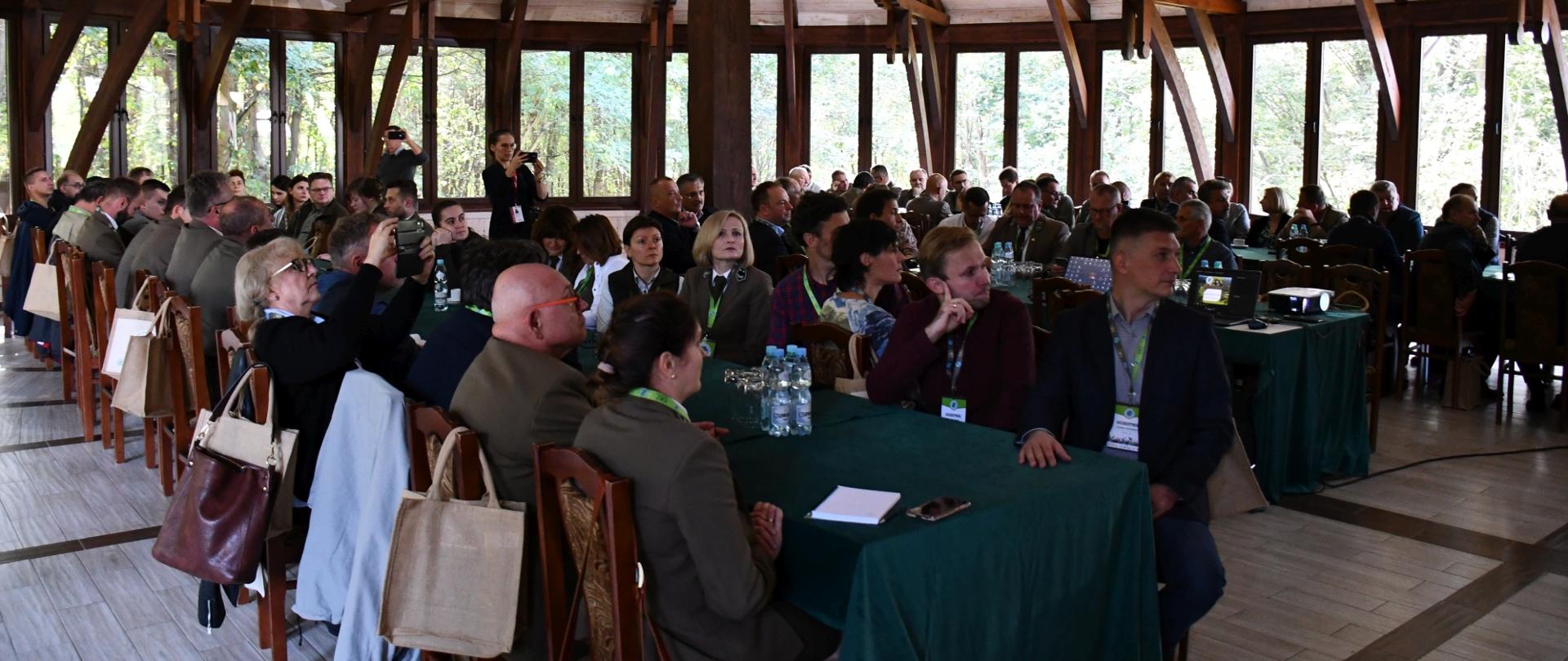 Uczestnicy konferencji siedzący przy długich stołach w sali konferencyjnej 
