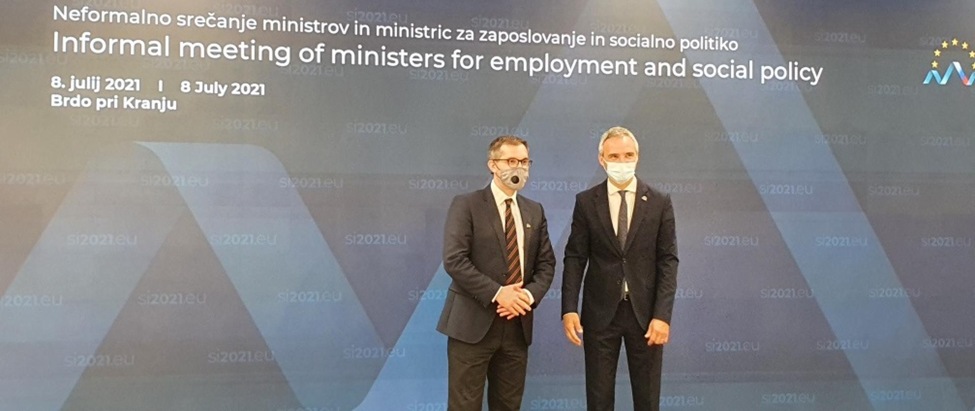 Wiceminister MRPiT Marek Niedużak stojący w masce na tle banneru z angielskim napisem informującym o nieformalnym spotkaniu ministrów pracy i polityki społecznej Unii Europejskiej, które odbywa się w Brdo, w Słowenii 8-9 lipca