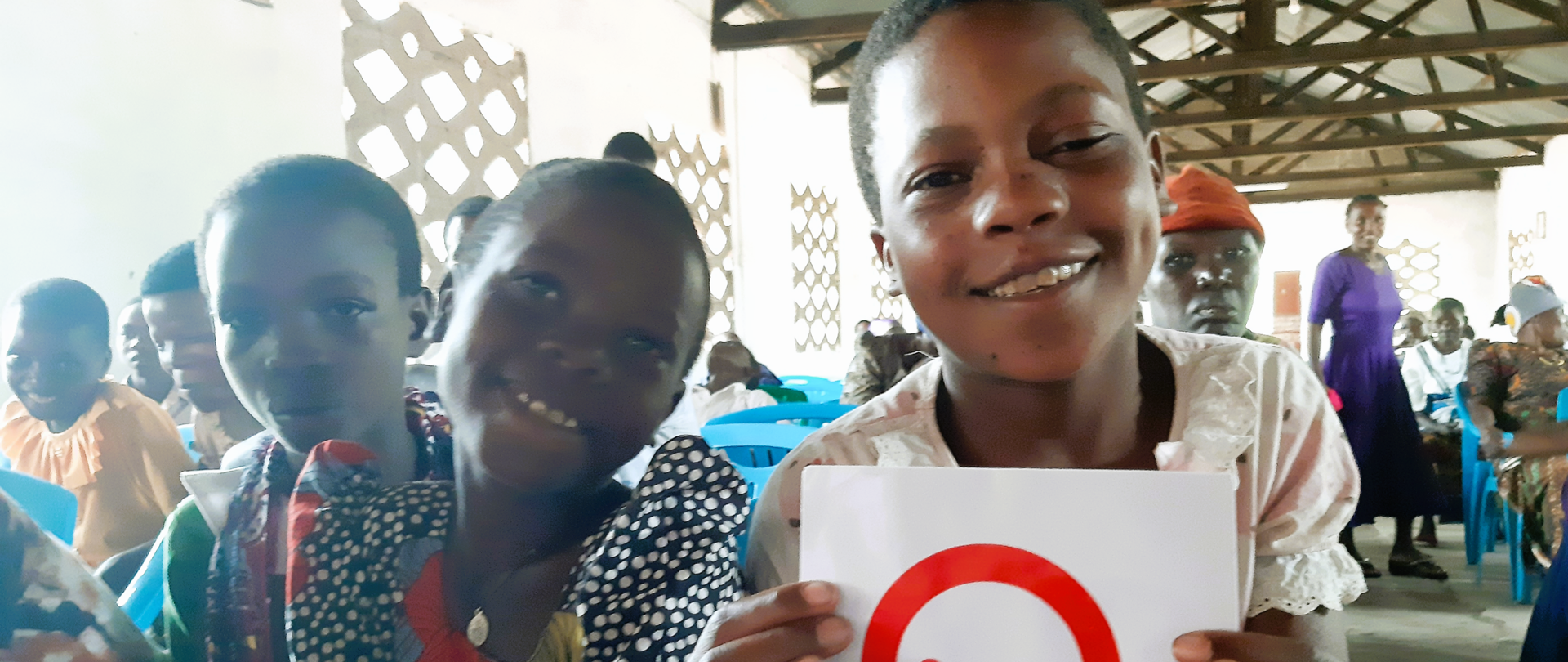 Troje czarnoskórych dzieci pozuje do zdjęcia. Jedno z nich trzyma wydrukowane logo polskiej pomocy.