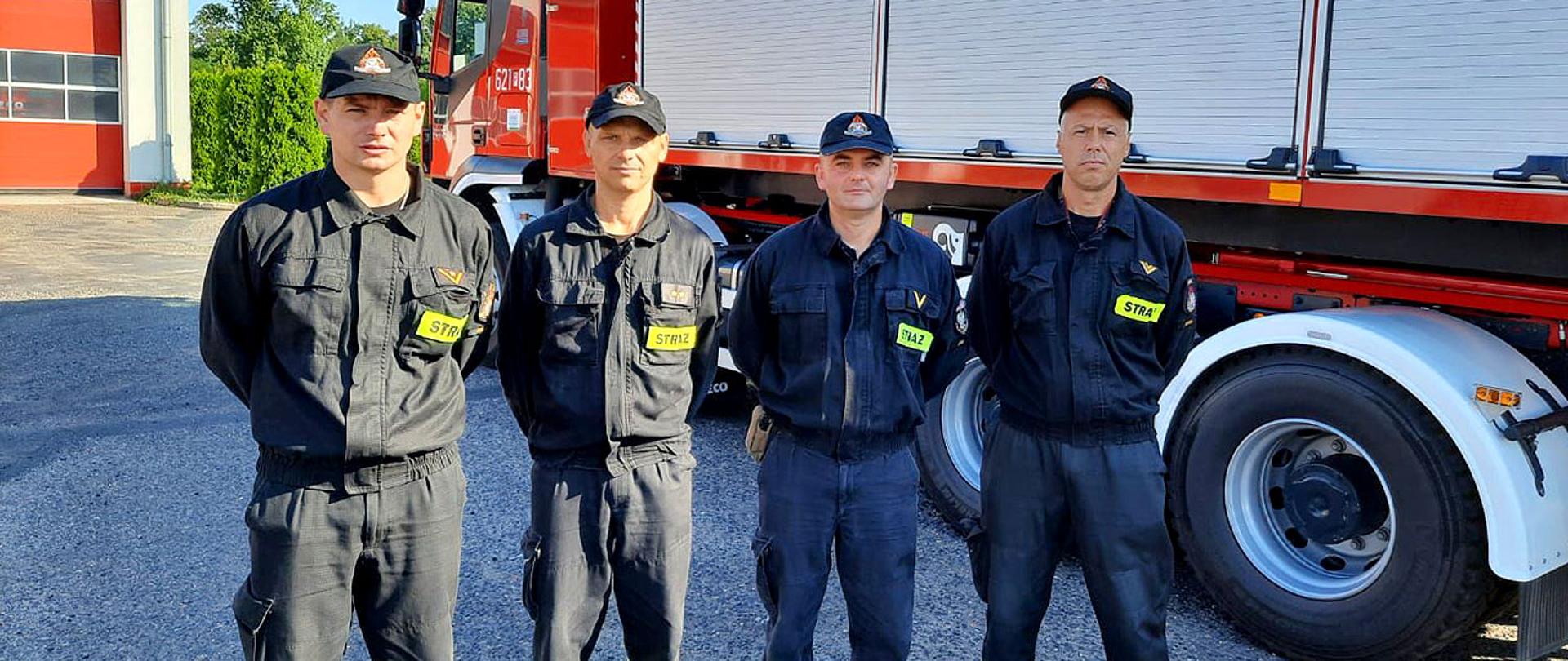 Czterech strażaków przed wyjazdem do Grecji. w tle samochód pożarniczy z kontenerami.