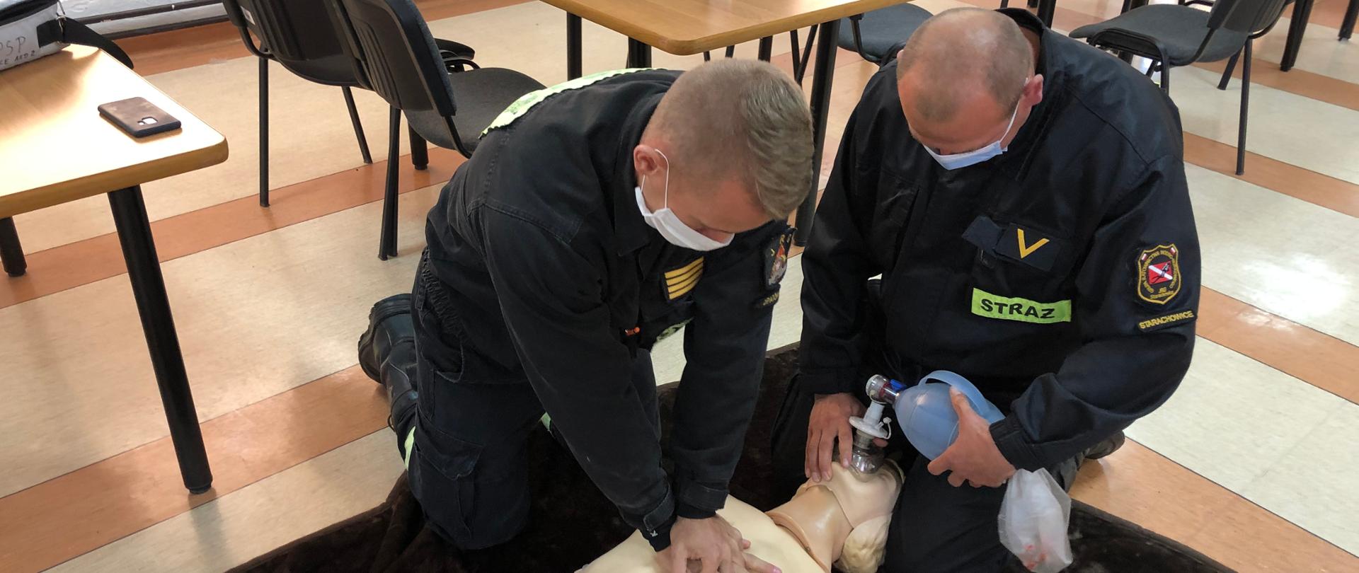 Na pierwszym zdjęciu strażacy-ratownicy wykonują symulację resuscytacji krążeniowo-oddechową u osoby dorosłej. Jeden z ratowników wykonuje 30 uciśnięć klatki piersiowej, natomiast drugi wykonuje 2 oddechy ratownicze za pomocą worka samorozprężalnego.