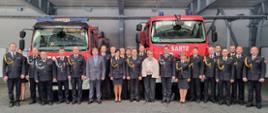 Zdjęcie grupowe uczestników uroczystej zbiórki, którzy stoją przed przekazywanymi samochodami ratowniczo –gaśniczymi 