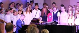 zdjęcie przedstawia chór szkolny wraz z prowadzącym akompaniatorem przy fortepianie na scenie sali koncertowej podczas wykonania utworu, inne ujęcie z bliska