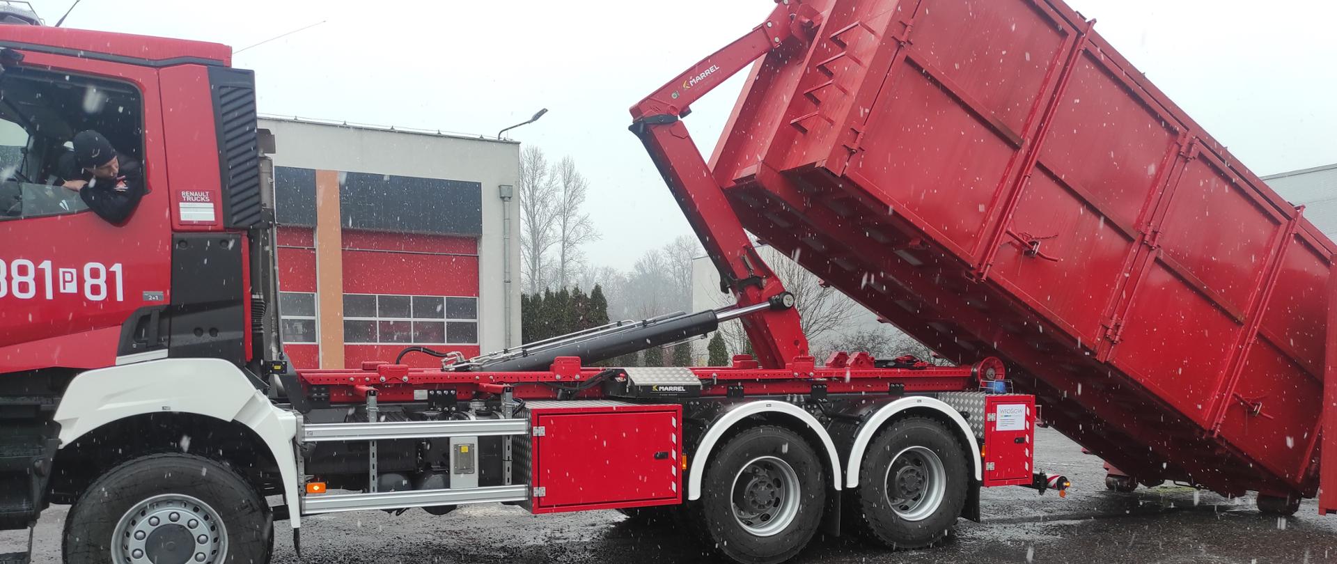 Samochód ciężarowy strażaki wciąga kontener na swoją platformę.