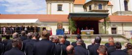 Widok z tyłu. Uczestnicy mszy polowej z okazji obchodów powiatowego dnia strażaka. W tle ołtarz, z przodu pododdział OSP. Po lewej stronie trybuna z gośćmi honorowymi. 