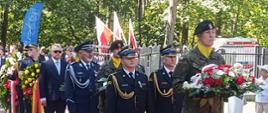 Przedstawiciele służb mundurowych oraz delegacje z wieńcami podczas uroczystości rocznicowych na terenie leśnym.