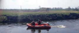 Strażak oraz przewodnik z psem tropiącym na łodzi przeszukują koryto rzeki w poszukiwaniu osoby zaginionej.
