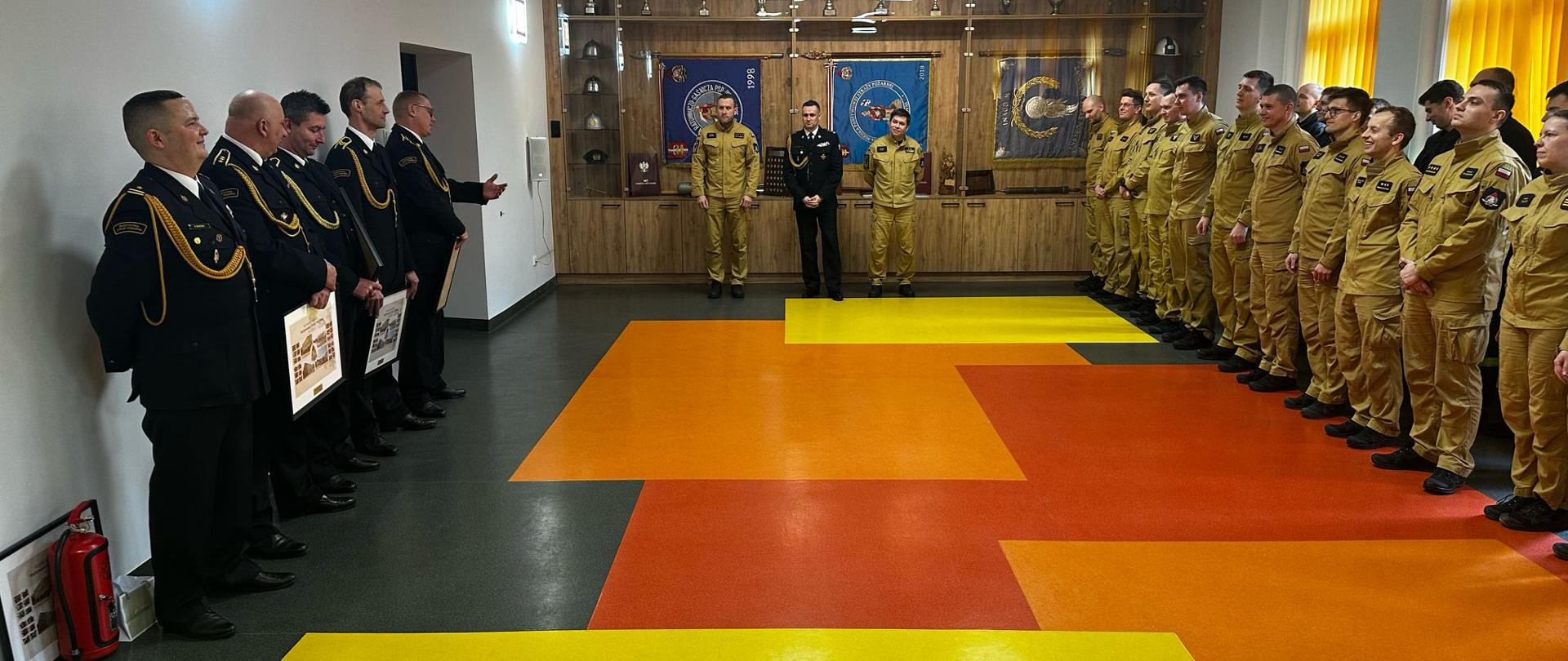 Zbiórka strażaków i pracowników komendy na sali tradycji. Po lewej stronie 5 funkcjonariuszy odchodzący na zaopatrzenie emerytalne. Po prawej stronie strażacy a na środku komendanci.
