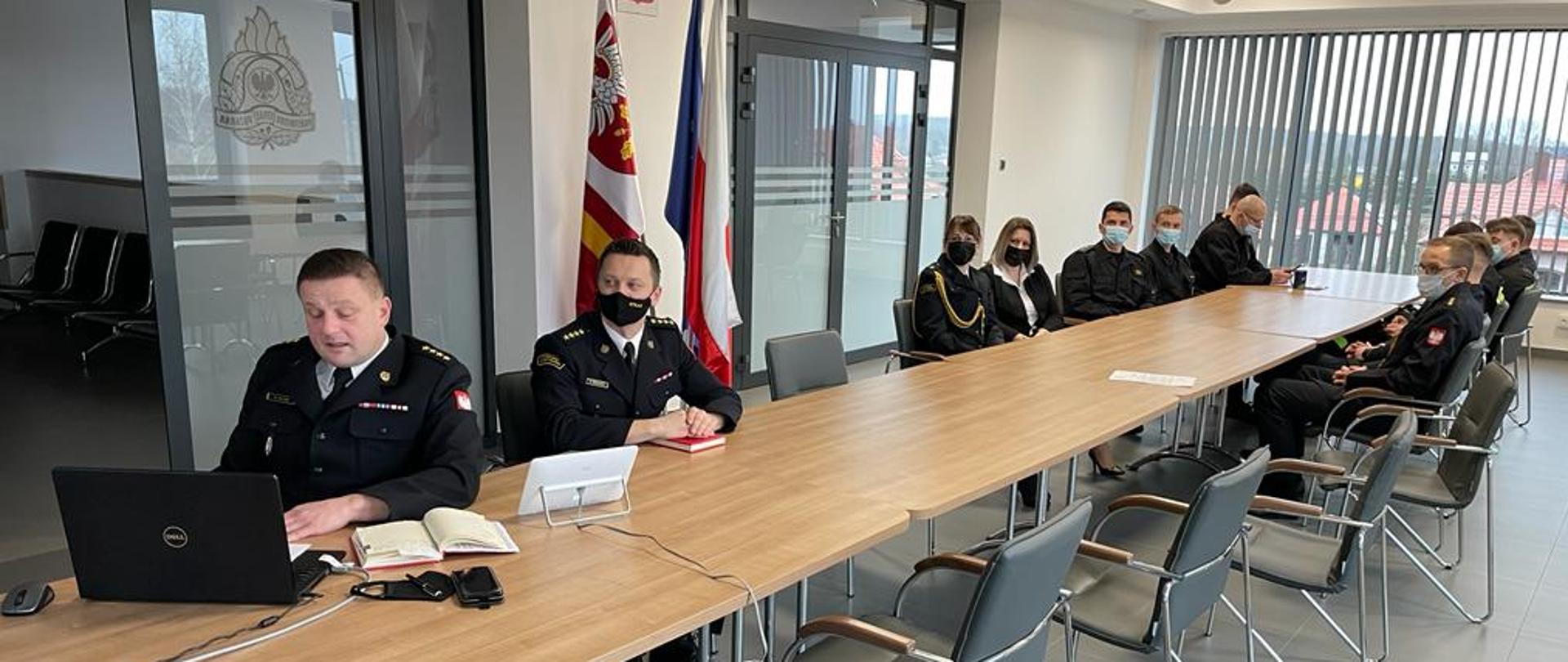 Na zdjęciu strażacy podczas narady siedzą przy stołach