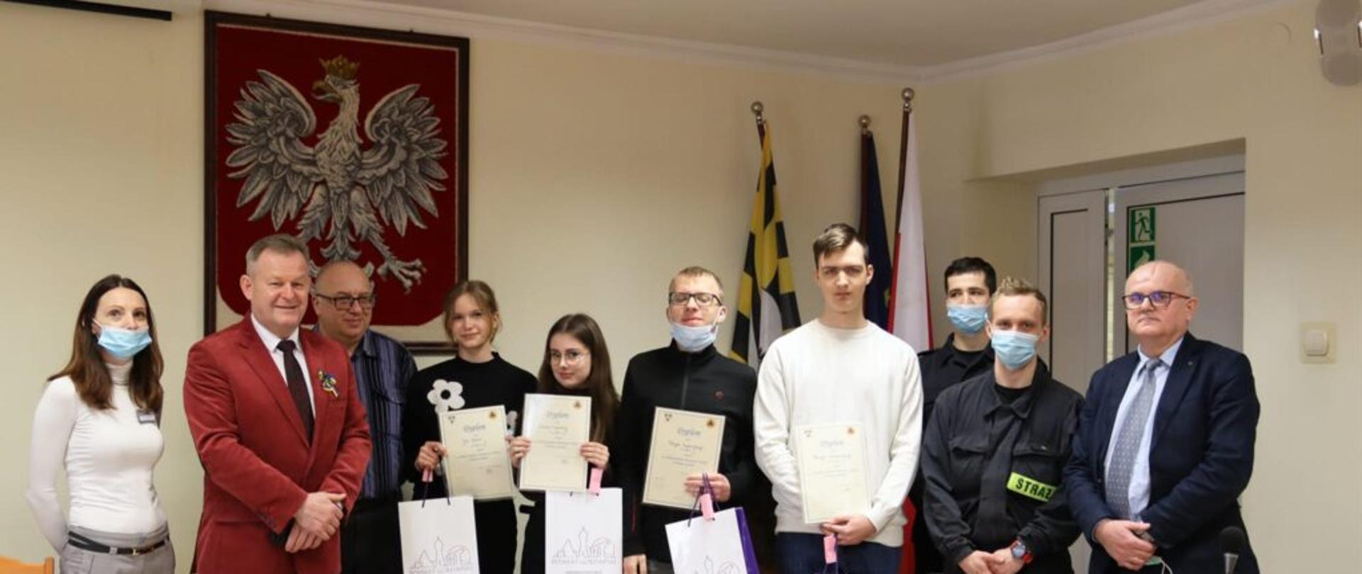 Zdjęcie przedstawia uczestników XXVI Wojewódzkiej Olimpiady Wiedzy o Obronie Cywilnej, pracowników Starostwa Powiatowego, przedstawicieli szkół ponadpodstawowych oraz strażaków Komendy Powiatowej Państwowej Straży Pożarnej po rozdaniu dyplomów i upominków