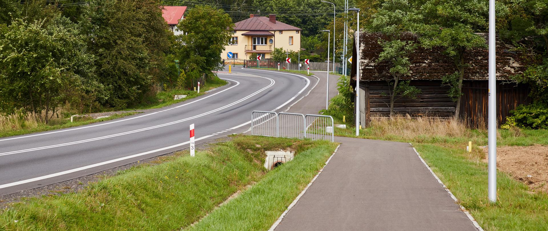 Na zdjęciu widać drogę a po jej prawej stronie chodnik. W oddali dom i zakręt.