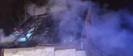 Na zdjęciu widać spaloną konstrukcję dachu i popękany od gorąca eternit. Na poddaszu znajduje się 2 strażaków z JRG Skarżysko-Kamienna, którzy prowadzą działania gaśnicze.