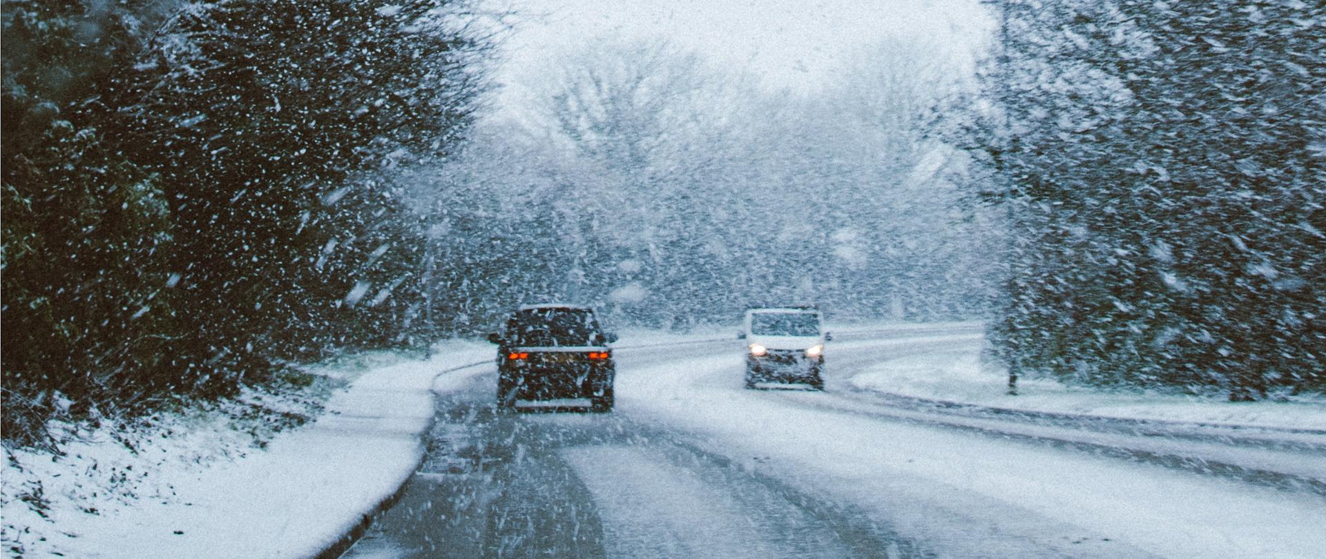 Samochody na zaśnieżonej drodze, przy padającym śniegu.
