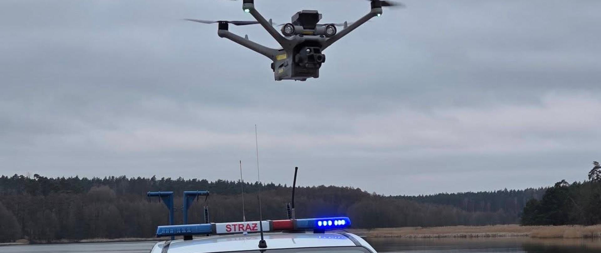 Zdjęcie przedstawia bezzałogowego statku powietrznego (tzw. drona) Komendy Powiatowej Państwowej Straży Pożarnej w Chodzieży podczas poszukiwania osoby zaginionej.
W tle tereny zielone.
