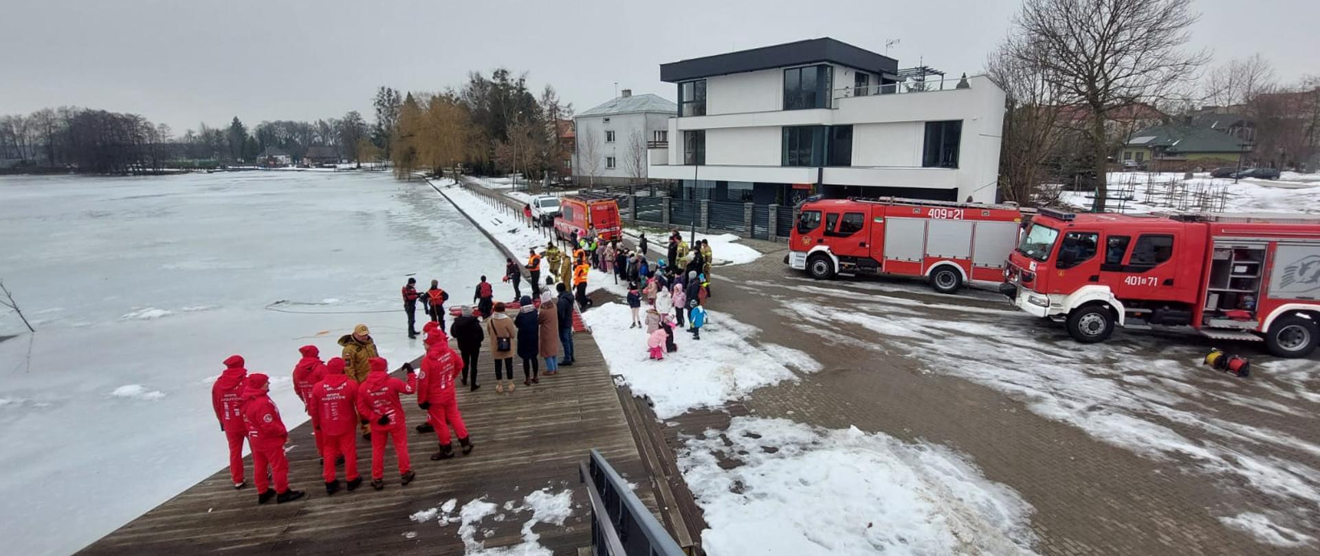 Na zdjęciu widać samochody strażacki, dzieci oraz strażaków podczas pokazów ratownictwa lodowego.