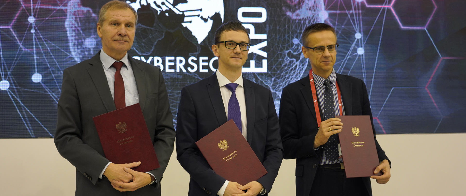 Trzech mężczyzn pozuje do wspólnego zdjęcia. Każdy z nich trzyma teczkę z napisem Ministerstwo Cyfryzacji