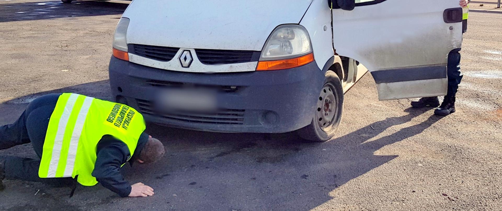 Akcja BUS w Wielkopolsce. Jeden z dostawczaków sprawdzany w punkcie kontroli. Na pierwszym planie zatrzymany pojazd. Jeden z inspektorów sprawdza podwozie. W tle radiowóz Inspekcji Transportu Drogowego. Za nim droga krajowa nr 32.