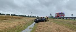 Dzień, opady deszczu. Samochód osobowy leżący na dachu w rowie poza jezdnią autostrady A2.