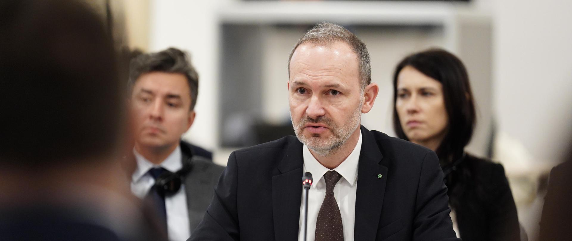 Na zdjęciu widać ministra Krzysztofa Hetmana, który zawiera głos na 9. posiedzeniu plenarnym Polsko-Ukraińskiej Komisji Międzyrządowej ds. Współpracy Gospodarczej. W tle uczestnicy posiedzenia. Minister wraz z innymi uczestnikami siedzi przy stole.