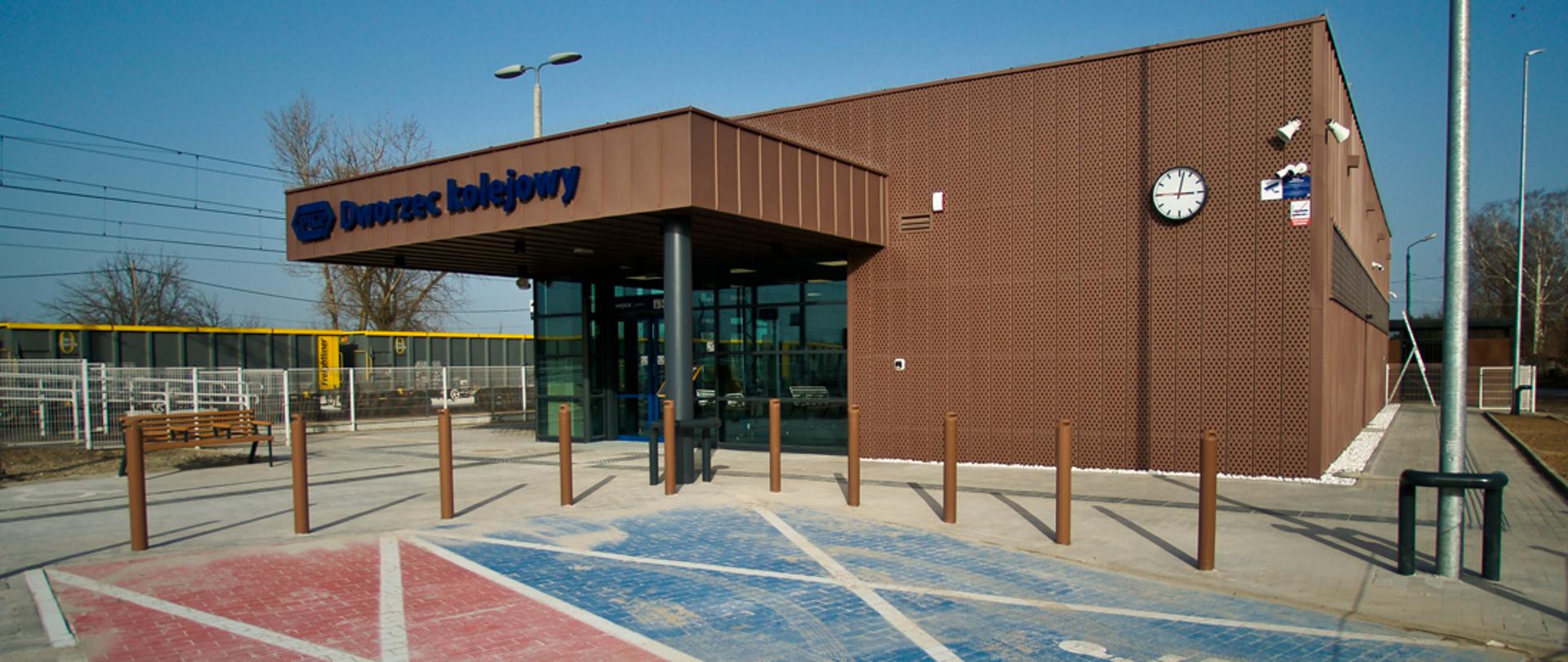 Budynek dworca kolejowego w Imbramowicach. Przed nim miejsca postojowe dla osób z niepełnosprawnościami.