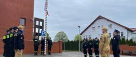 strażacy stoją wokół masztu na który wciągana jest flaga RP