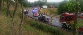 Na zdjęciu widać uszkodzony pojazd, trzy samochody strażackie, karetkę pogotowia oraz strażaków.